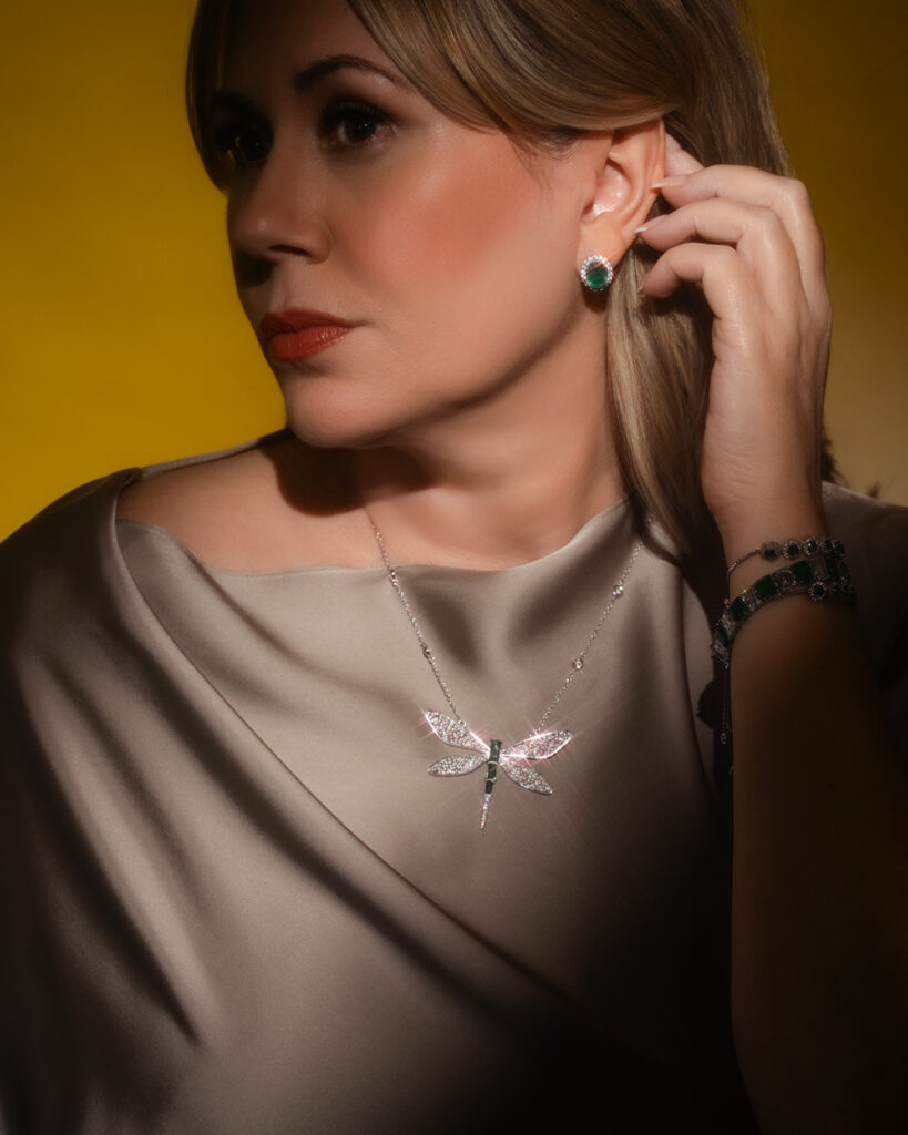 Darla wearing a champagne satin dress, dragonfly necklace, and emerald jewelry in a dramatically lit branding portrait.